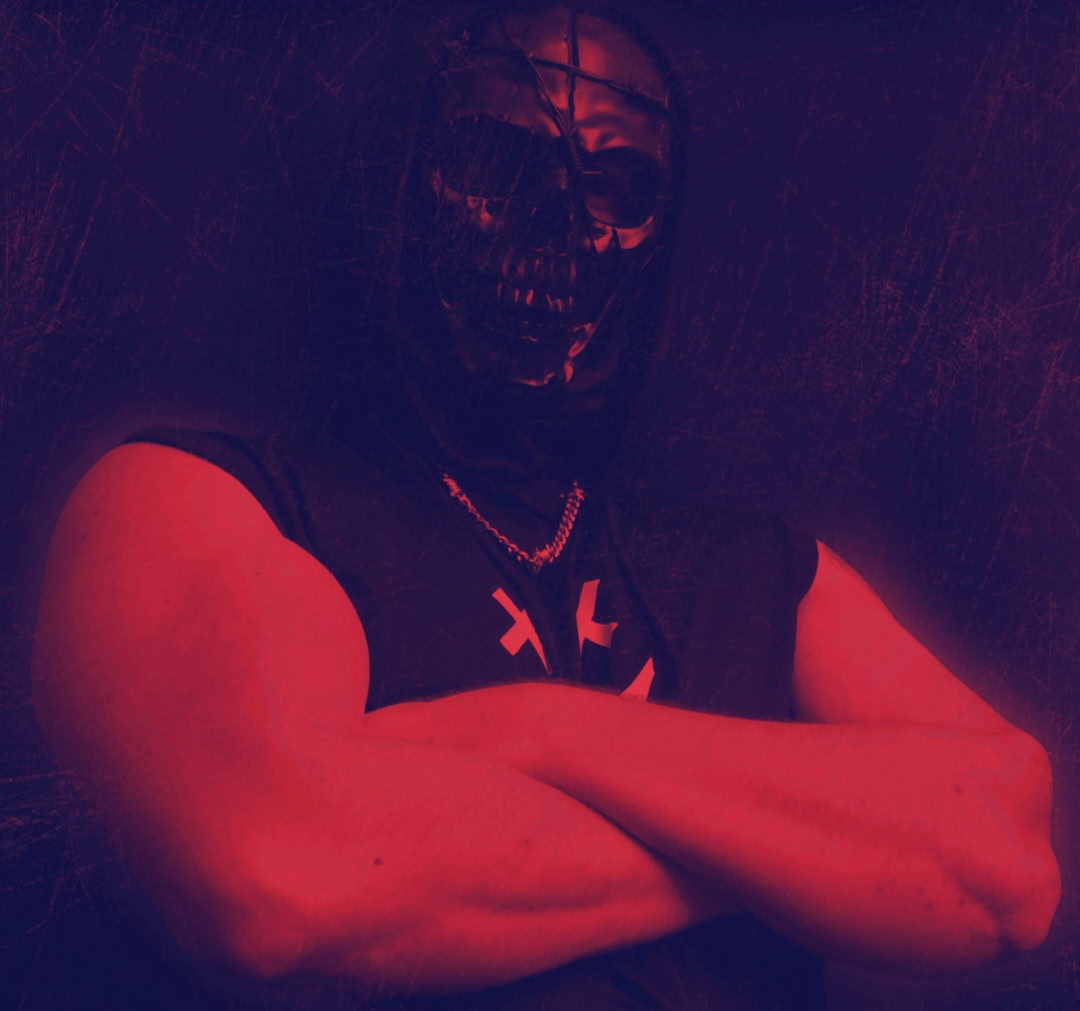Author Michael Wellington wearing a black skull mask with his bare muscular arms folded across his chest.